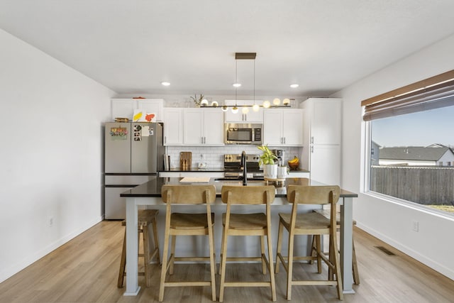 kitchen featuring visible vents, decorative backsplash, appliances with stainless steel finishes, white cabinets, and a kitchen island with sink