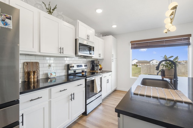 kitchen featuring a sink, stainless steel appliances, dark countertops, tasteful backsplash, and light wood-type flooring