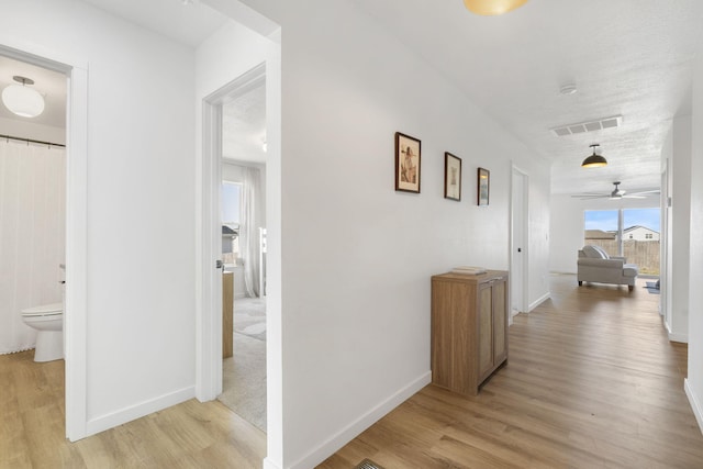 corridor featuring visible vents, light wood-style flooring, a textured ceiling, and baseboards