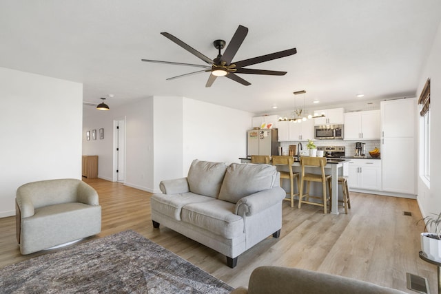 living area featuring visible vents, baseboards, recessed lighting, light wood-style floors, and ceiling fan with notable chandelier