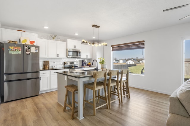 kitchen with a sink, dark countertops, stainless steel appliances, light wood-style floors, and decorative backsplash