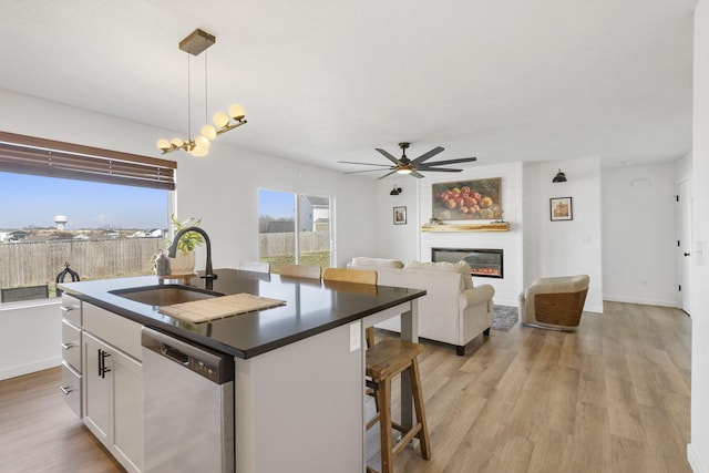 kitchen with dishwasher, dark countertops, light wood-style flooring, and a sink