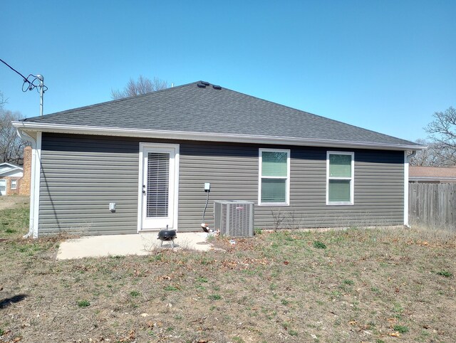 back of property featuring a yard, central air condition unit, roof with shingles, and fence