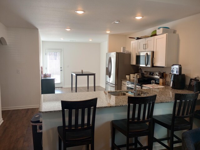 kitchen featuring visible vents, dark wood finished floors, a breakfast bar area, light stone counters, and appliances with stainless steel finishes