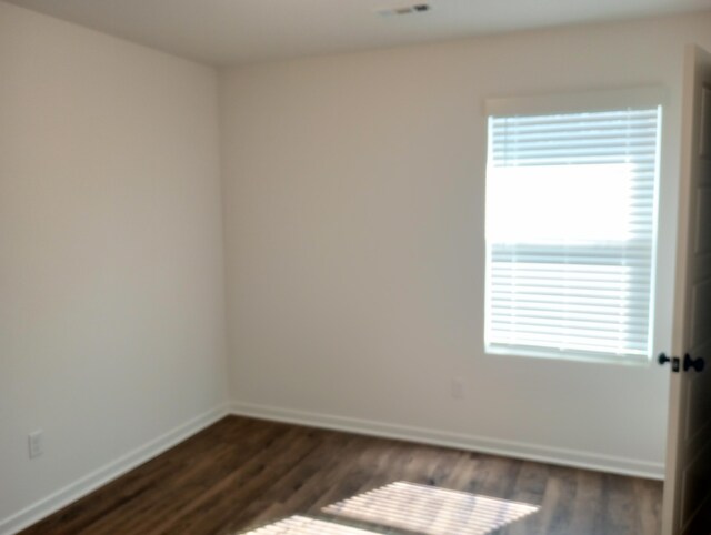 spare room featuring baseboards, a healthy amount of sunlight, and dark wood-style floors