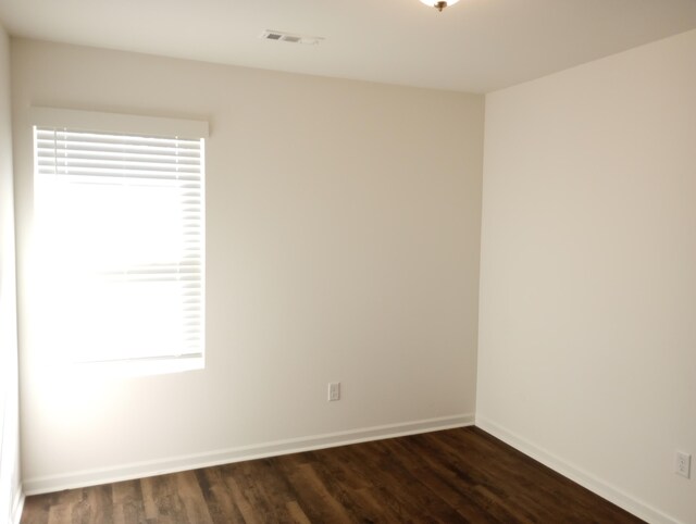 spare room featuring dark wood finished floors, visible vents, and baseboards