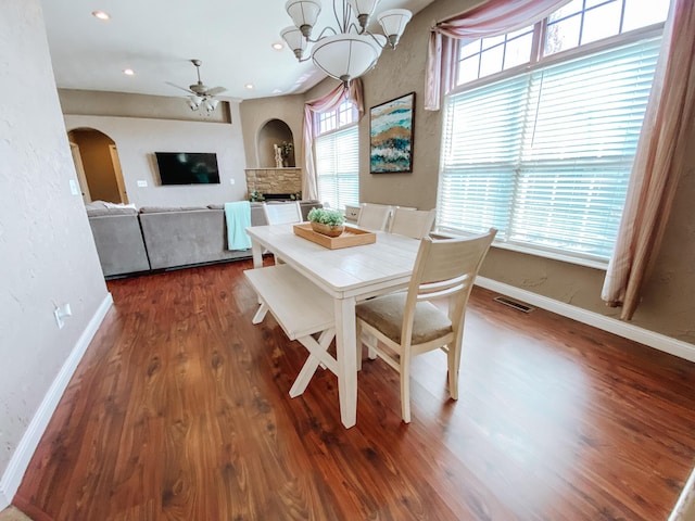 dining space featuring baseboards, arched walkways, wood finished floors, and ceiling fan with notable chandelier