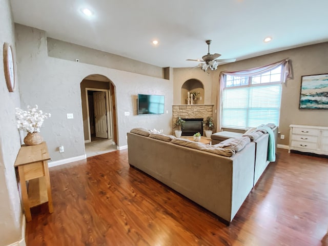 living area featuring wood finished floors, arched walkways, a fireplace, baseboards, and ceiling fan