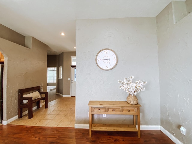 corridor featuring recessed lighting, a textured wall, baseboards, and light wood finished floors