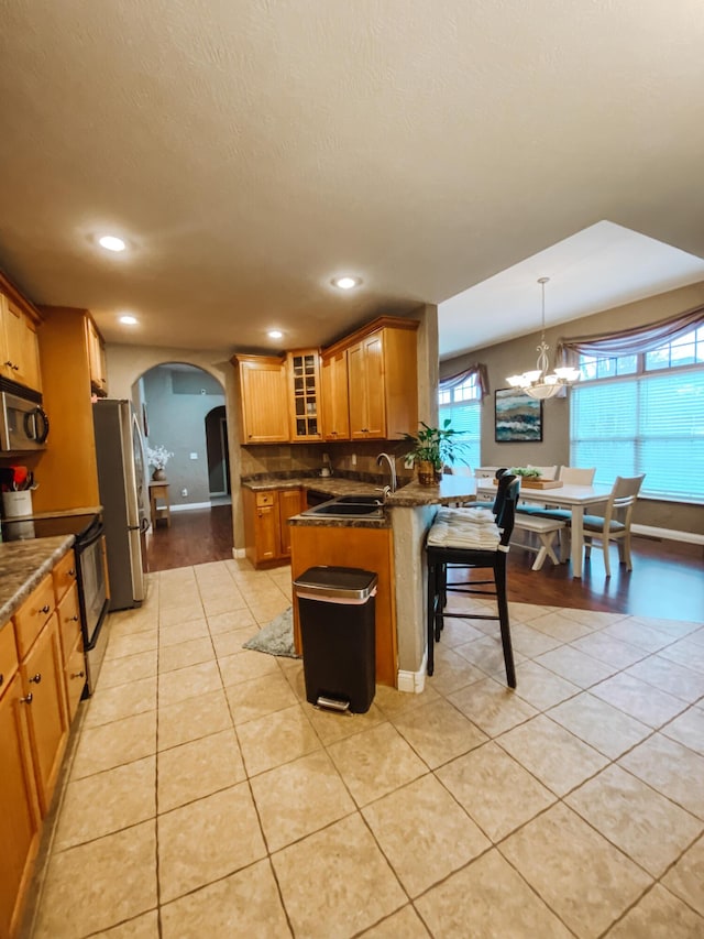 kitchen with light tile patterned flooring, arched walkways, a sink, stainless steel appliances, and glass insert cabinets