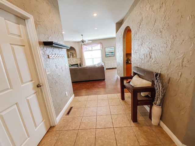 corridor featuring arched walkways, visible vents, light tile patterned floors, and a textured wall