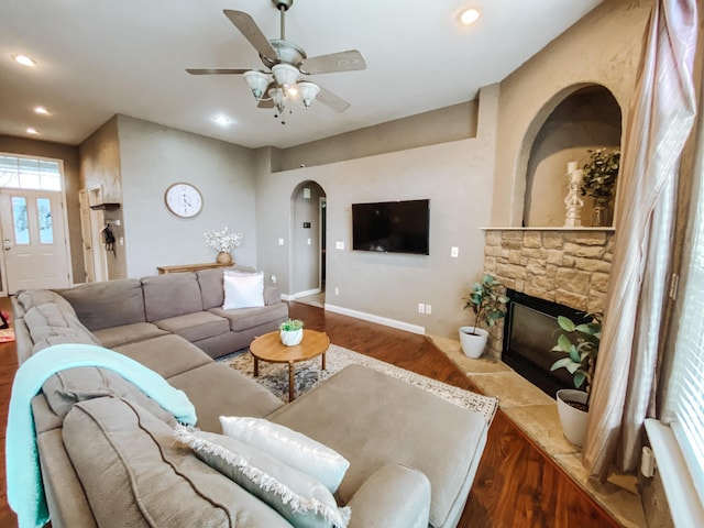 living room with a ceiling fan, wood finished floors, recessed lighting, arched walkways, and a stone fireplace