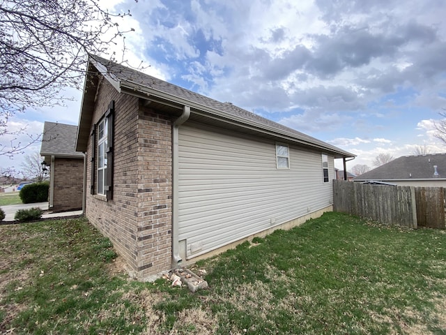 view of property exterior featuring brick siding, a yard, and fence