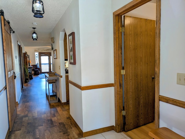 hall featuring a barn door, baseboards, a textured ceiling, and wood finished floors