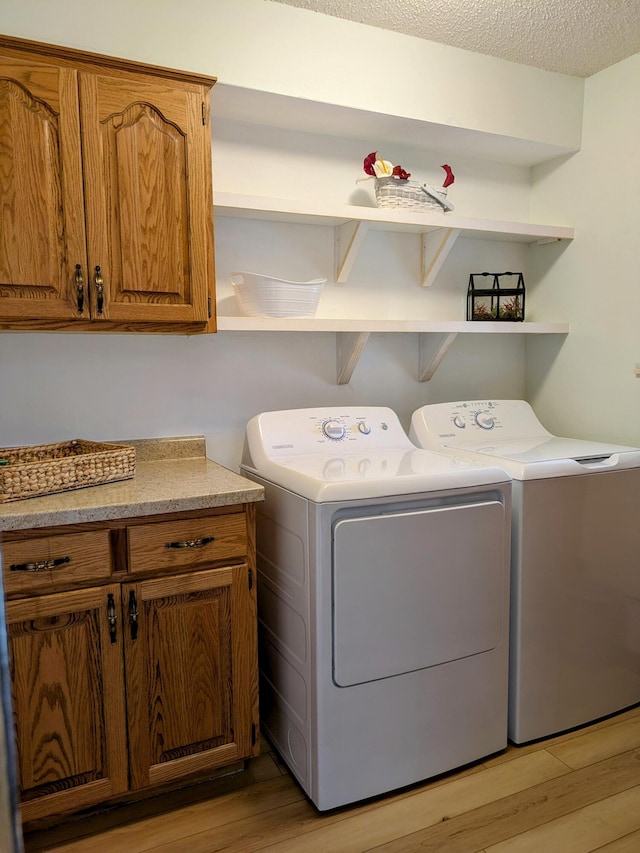 laundry area with light wood finished floors, cabinet space, a textured ceiling, and washer and clothes dryer