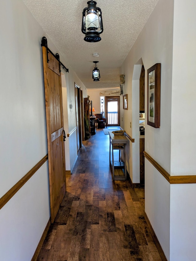 corridor with a barn door, dark wood-type flooring, a textured ceiling, and baseboards