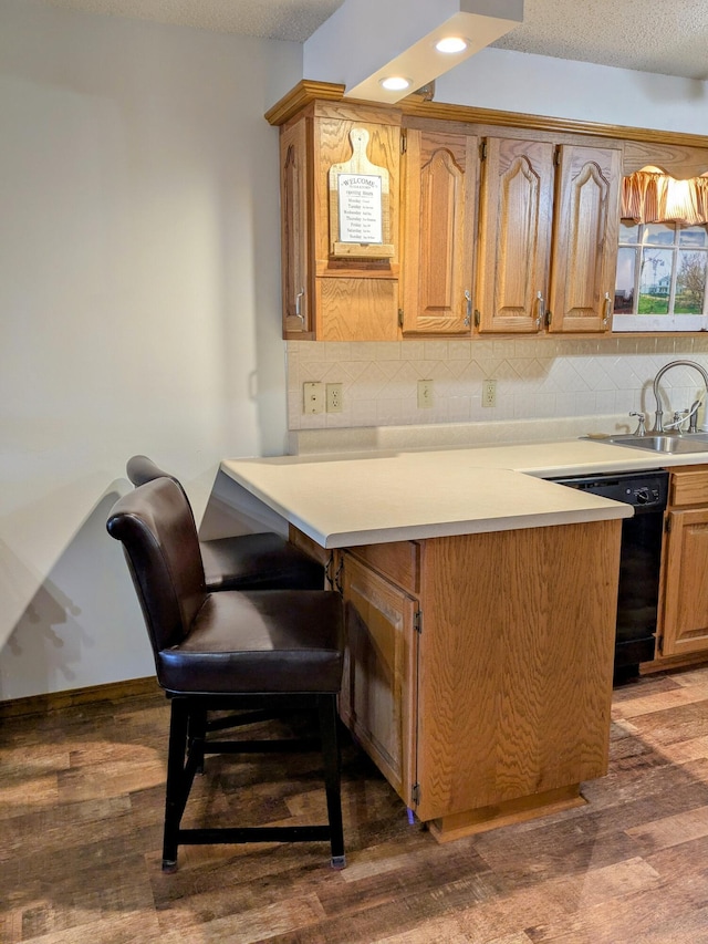 kitchen featuring wood finished floors, a sink, light countertops, black dishwasher, and backsplash