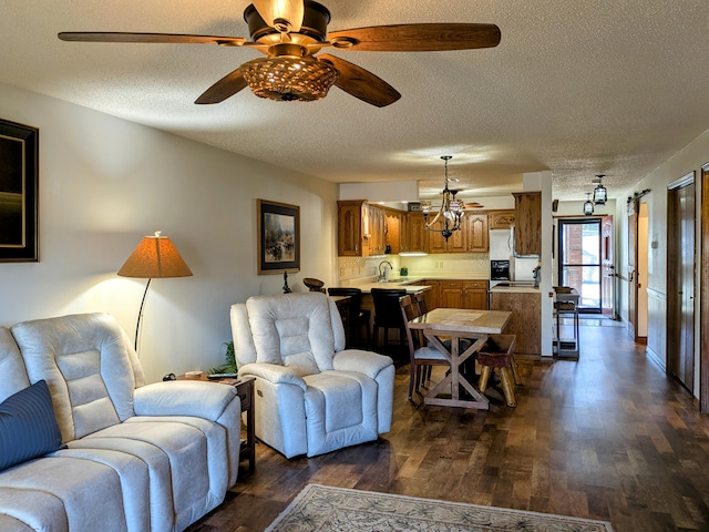 living room with ceiling fan with notable chandelier, dark wood-style flooring, and a textured ceiling