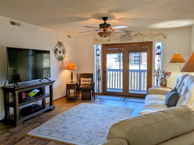 living area featuring wood finished floors, a ceiling fan, visible vents, and a textured ceiling