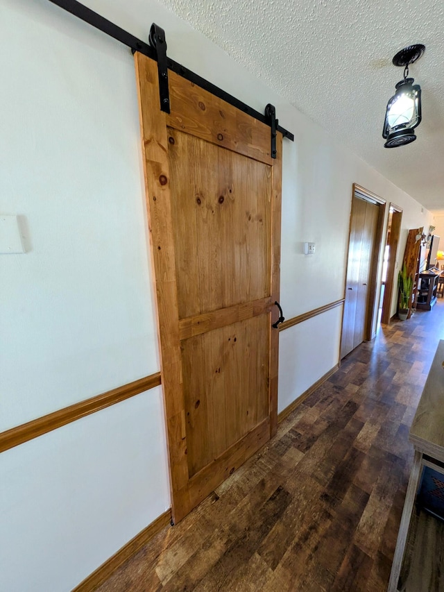 hallway featuring a barn door, dark wood-style floors, baseboards, and a textured ceiling