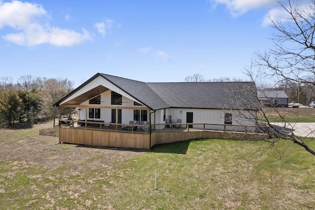 rear view of house with a yard, a wooden deck, and roof with shingles