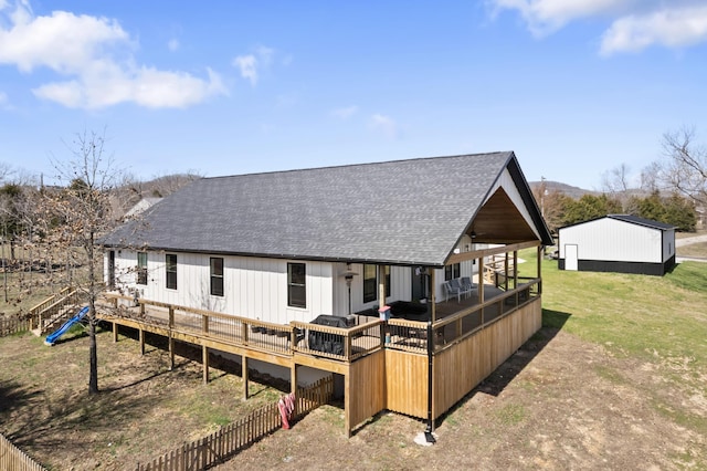 back of property with a yard, roof with shingles, and a wooden deck