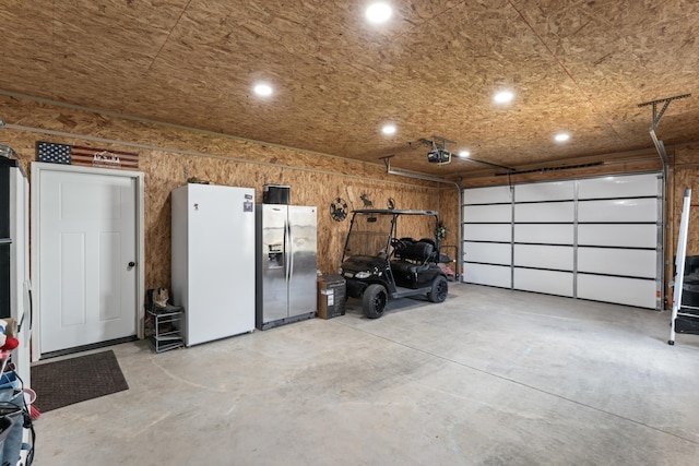 garage with a garage door opener, stainless steel refrigerator with ice dispenser, and freestanding refrigerator