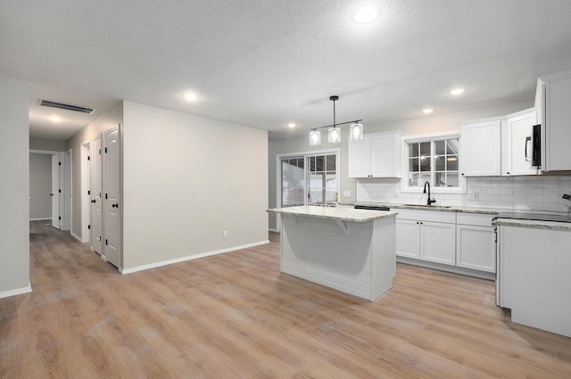 kitchen featuring visible vents, backsplash, a center island, light wood-style floors, and a sink