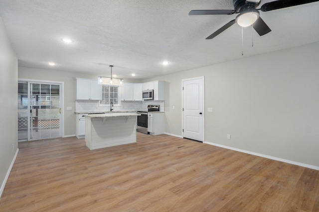 kitchen featuring a kitchen island, light wood-style floors, appliances with stainless steel finishes, white cabinets, and decorative backsplash