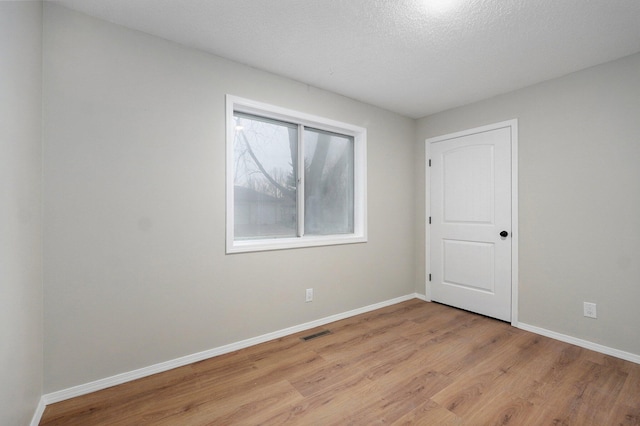 unfurnished room featuring baseboards, visible vents, light wood finished floors, and a textured ceiling