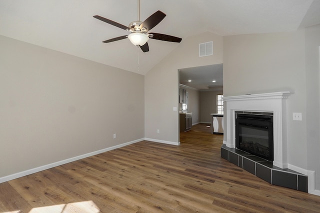 unfurnished living room featuring visible vents, a tiled fireplace, wood finished floors, baseboards, and ceiling fan