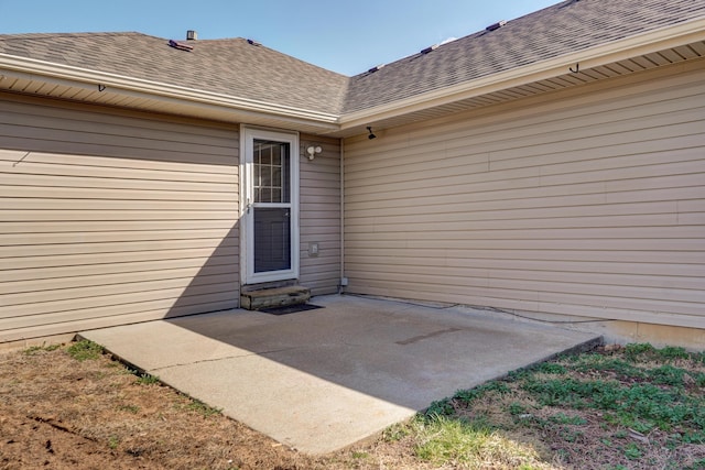 entrance to property featuring a patio area and roof with shingles