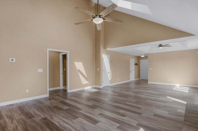 unfurnished living room with baseboards, ceiling fan, a skylight, wood finished floors, and high vaulted ceiling