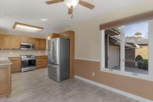 kitchen with light stone counters, baseboards, ceiling fan, stainless steel appliances, and tasteful backsplash