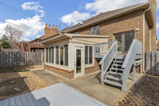 rear view of house featuring a deck, a fenced backyard, brick siding, and a sunroom