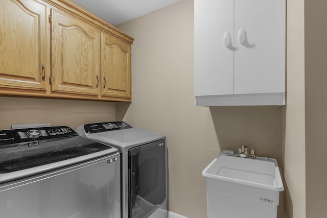 clothes washing area featuring washing machine and clothes dryer, cabinet space, and a sink