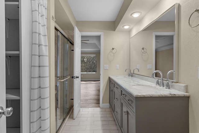 bathroom featuring a shower stall, double vanity, baseboards, and a sink