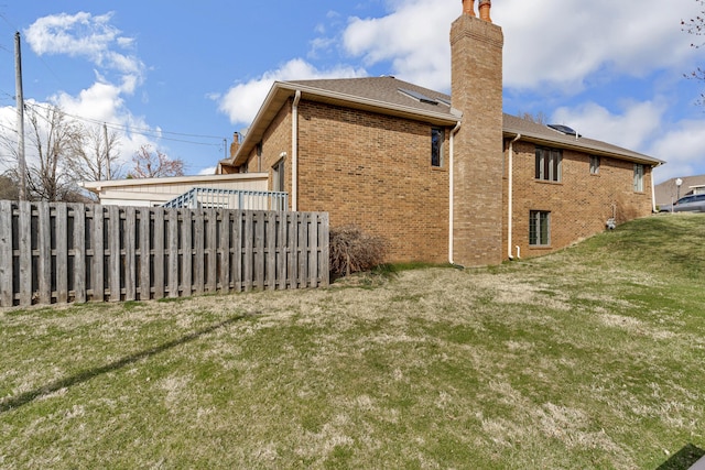 back of house with brick siding, a lawn, a chimney, and fence