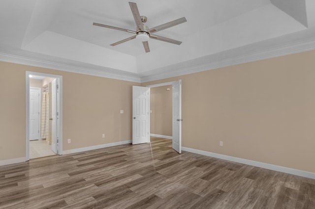 empty room with ceiling fan, a tray ceiling, and wood finished floors