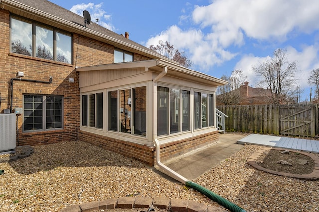 back of property featuring fence, cooling unit, a sunroom, brick siding, and a patio area