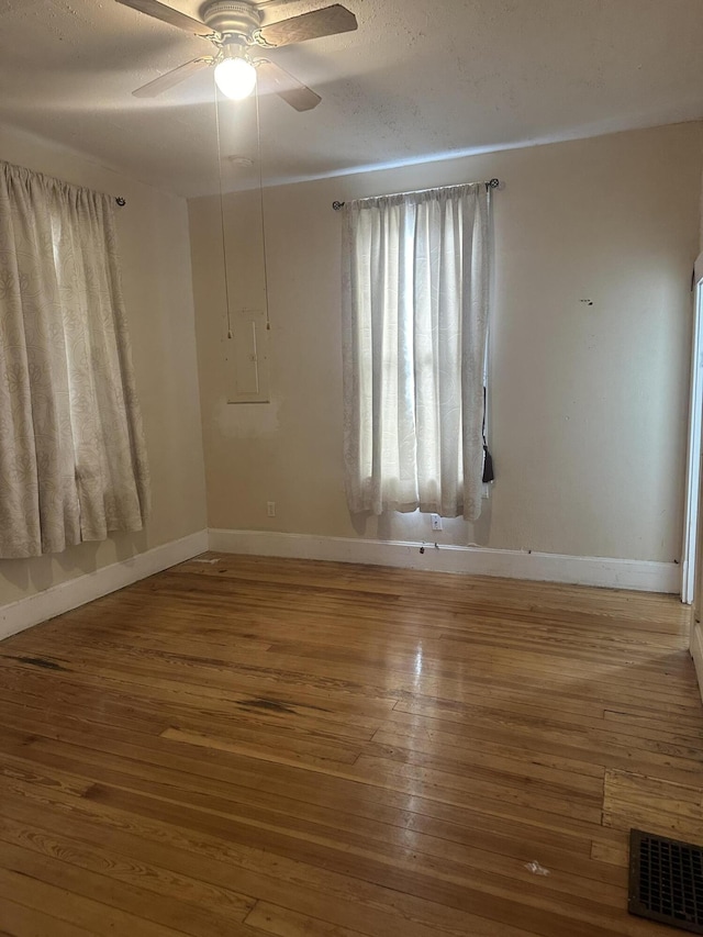 empty room with a ceiling fan, wood finished floors, visible vents, and baseboards