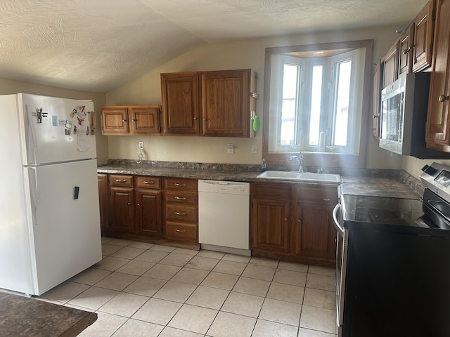 kitchen with light tile patterned floors, lofted ceiling, a sink, stainless steel appliances, and dark countertops