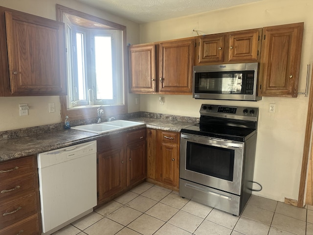 kitchen with a sink, dark countertops, appliances with stainless steel finishes, and light tile patterned flooring