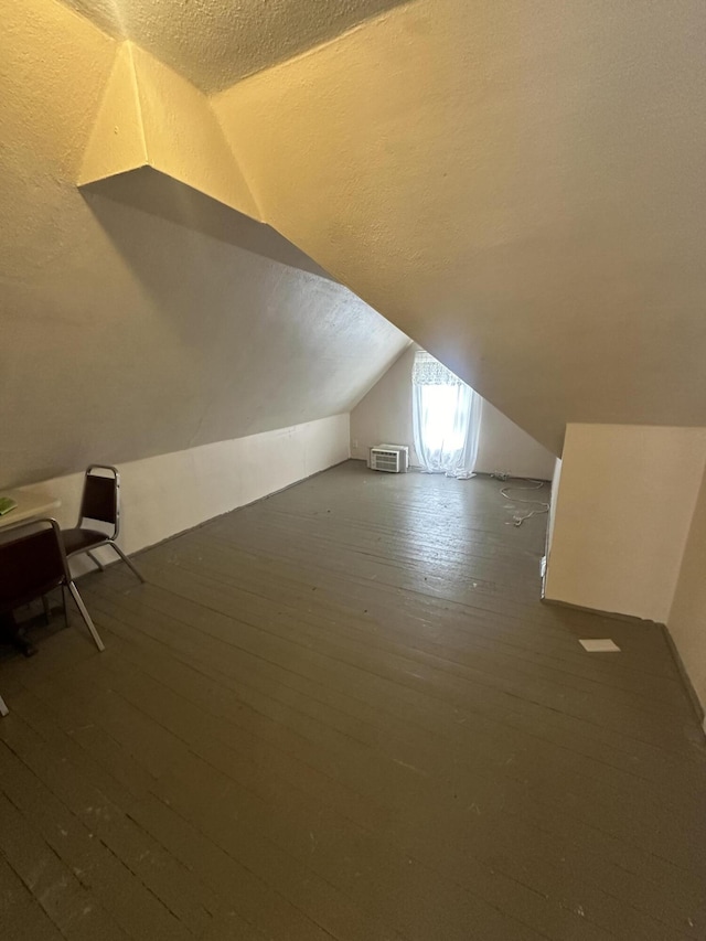 additional living space with a textured ceiling, lofted ceiling, and wood-type flooring