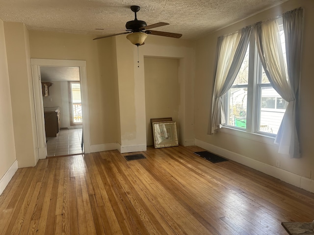 spare room with visible vents, a textured ceiling, light wood-style flooring, and a ceiling fan