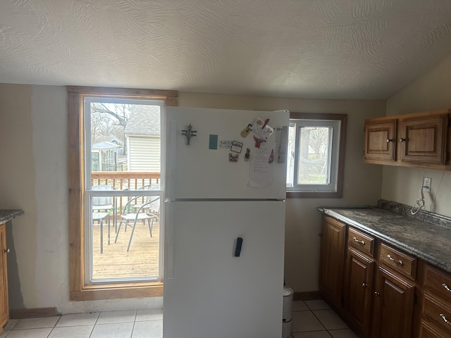 kitchen featuring dark countertops, light tile patterned floors, freestanding refrigerator, and a textured ceiling