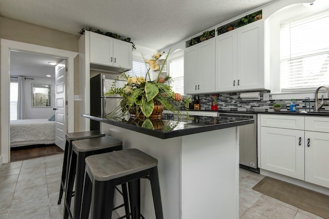 kitchen featuring a breakfast bar, dark countertops, stainless steel appliances, white cabinets, and decorative backsplash