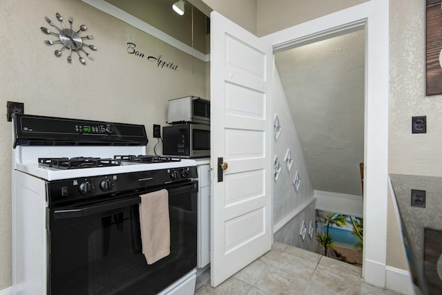 kitchen with gas stove, stainless steel microwave, and light tile patterned floors