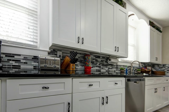 kitchen featuring stainless steel dishwasher, dark countertops, white cabinets, and a sink