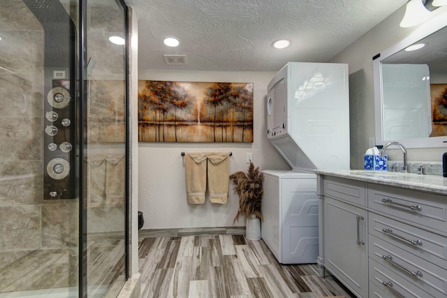 full bath with a stall shower, vanity, stacked washer / drying machine, and wood finished floors